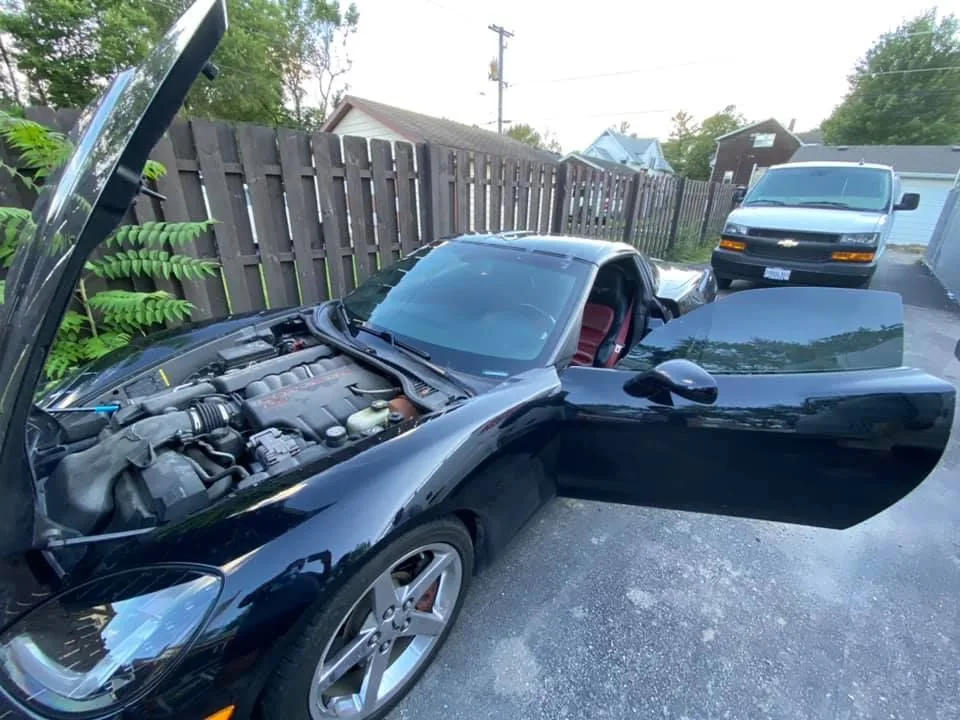 A black sports car with its hood up and doors open.
