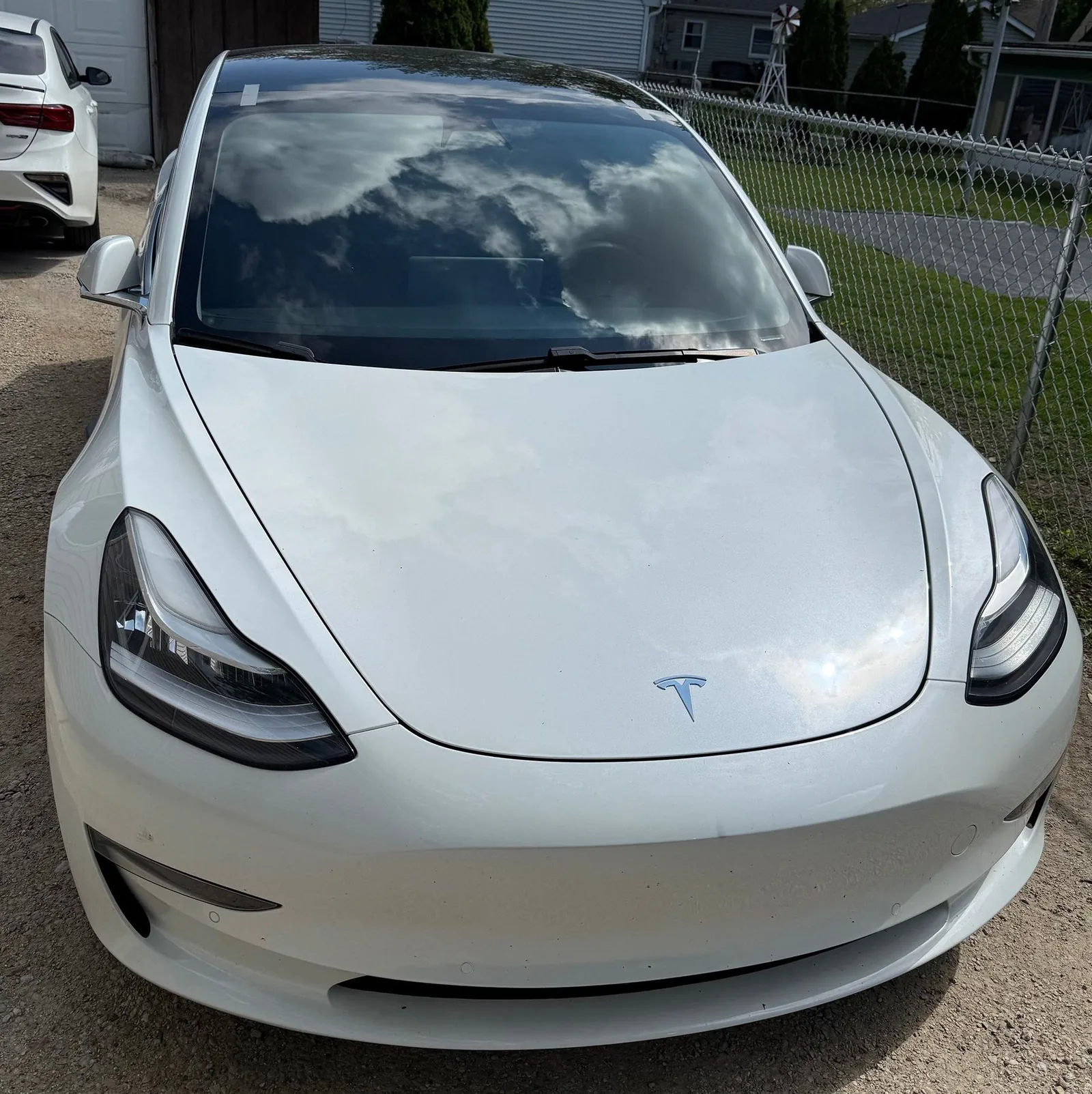 A white Tesla Model 3 parked in a driveway next to a fence.